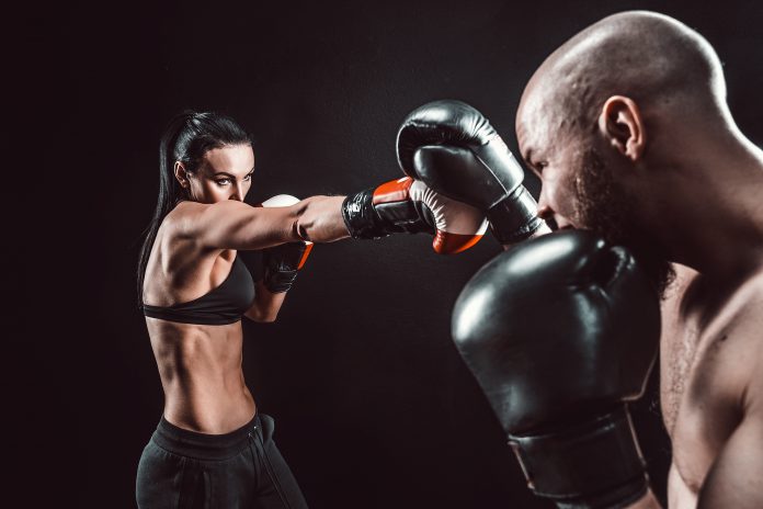 Shirtless Woman exercising with trainer at boxing and self defense lesson, studio, smoke on background. Female and male fight